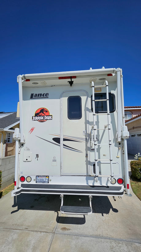 Rear view of a white Lance truck camper, decorated with a Jurassic Park decal, ready for your next RV rental trip.