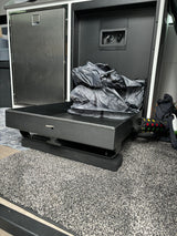 Compact RV rental interior featuring a mini-fridge, water hookups, and pull-out storage with gear on a textured floor.