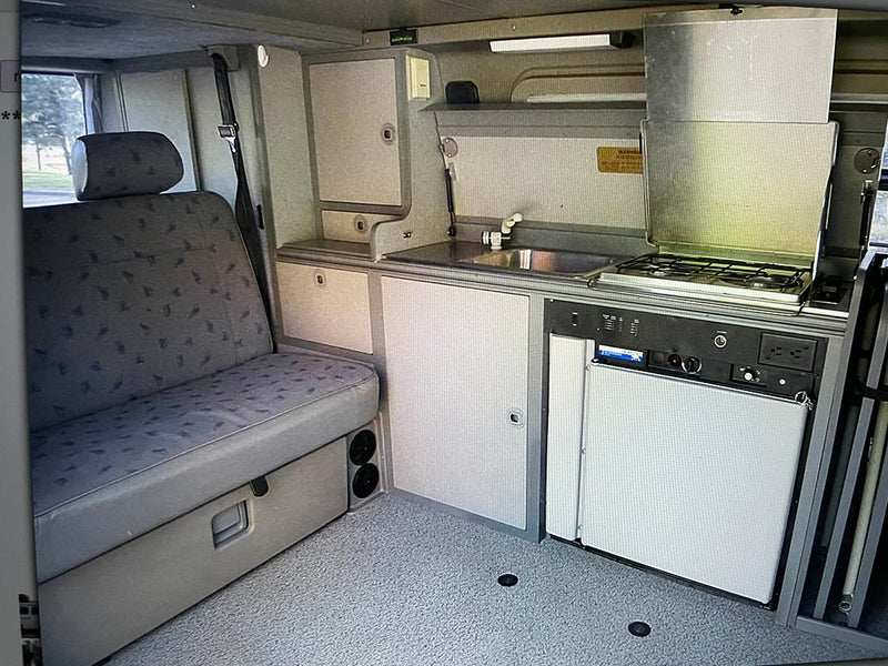  parked on a sunlit road lined with tall trees.|RV rental interior: versatile living space with bench seating — photo 5