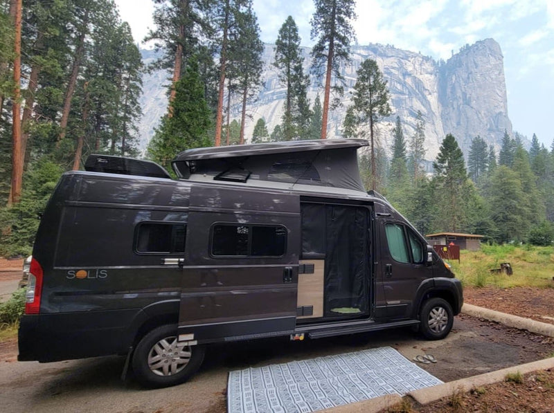 This Winnebago Solis RV rental is parked at a scenic forest campsite with a massive granite mountain backdrop — photo 1