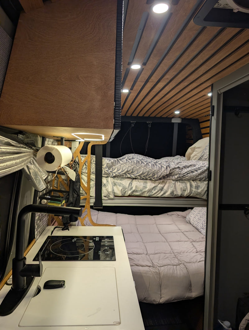 Compact rv rental interior with a functional kitchenette, induction cooktop, and cozy bunk beds. Wooden ceiling and ambient lighting in this camper van. — photo 18