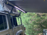 Adventure-ready RV rental: Jeep Gladiator with rooftop tent & awning setup in a lush forest for camping.