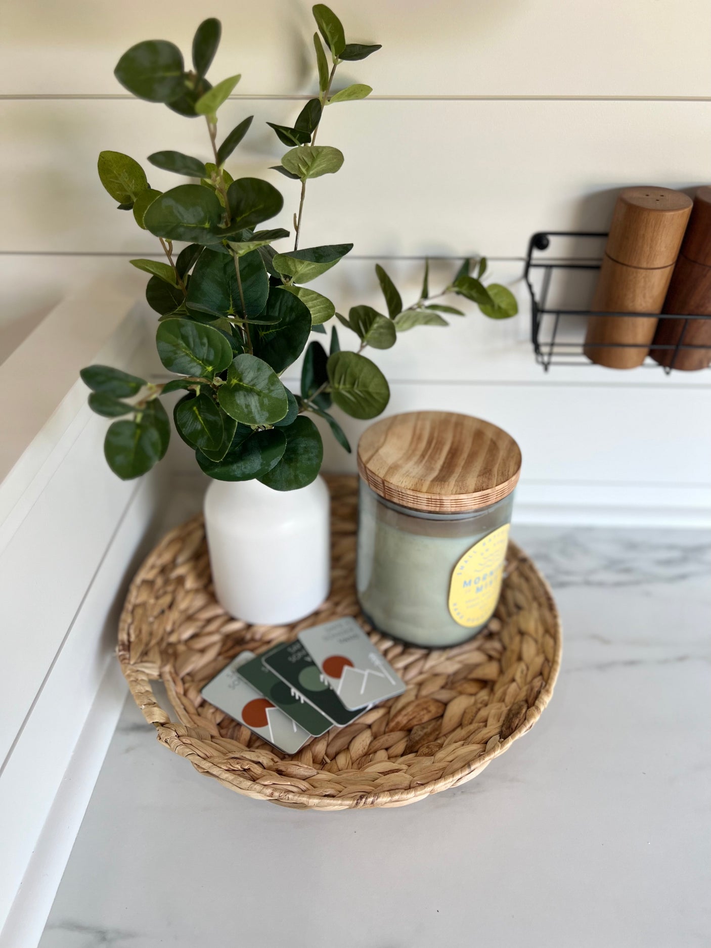 Cozy RV rental decor: green plant, candle, and decorative cards on a woven tray. Kitchen shakers visible.