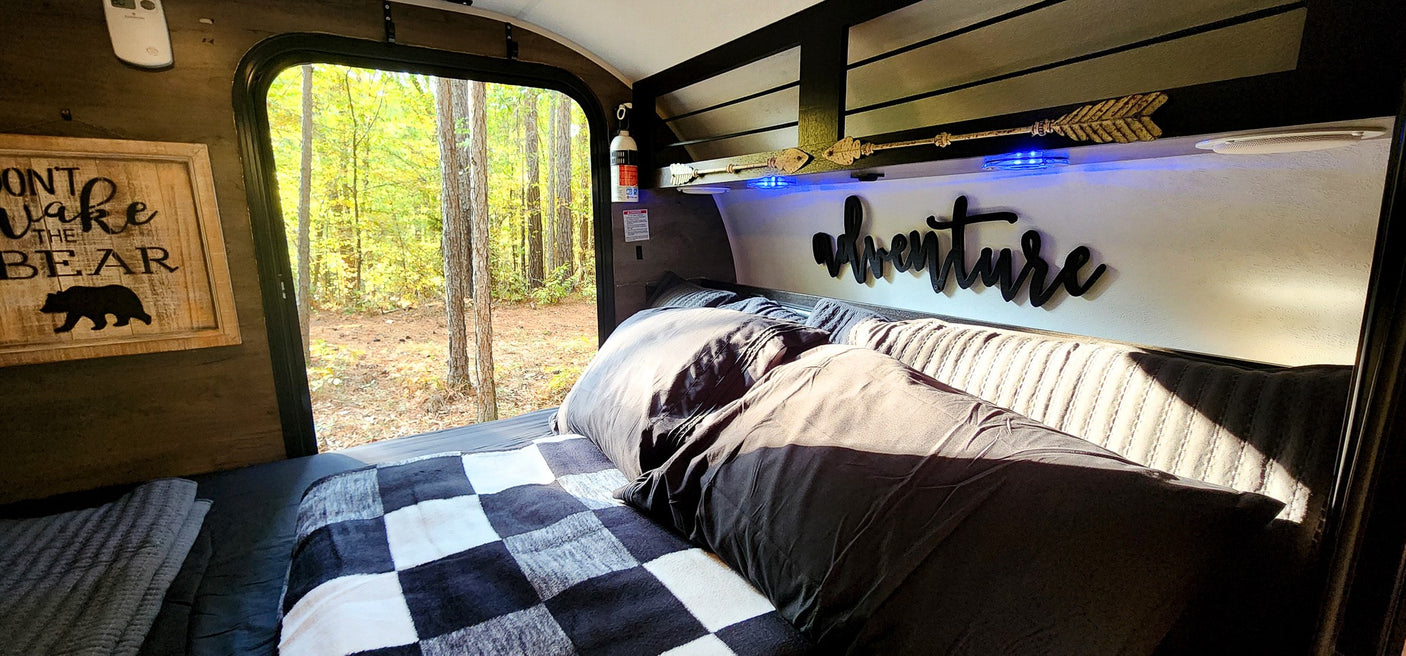 Cozy RV rental interior: bed, forest view, 'Don't Wake the Bear' sign, and 'adventure' decor.