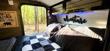 Cozy RV rental interior: bed, forest view, 'Don't Wake the Bear' sign, and 'adventure' decor.