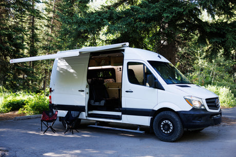 This white Mercedes Sprinter camper van, perfect for rv rental trips, is ready for camping with its side door open and awning extended.