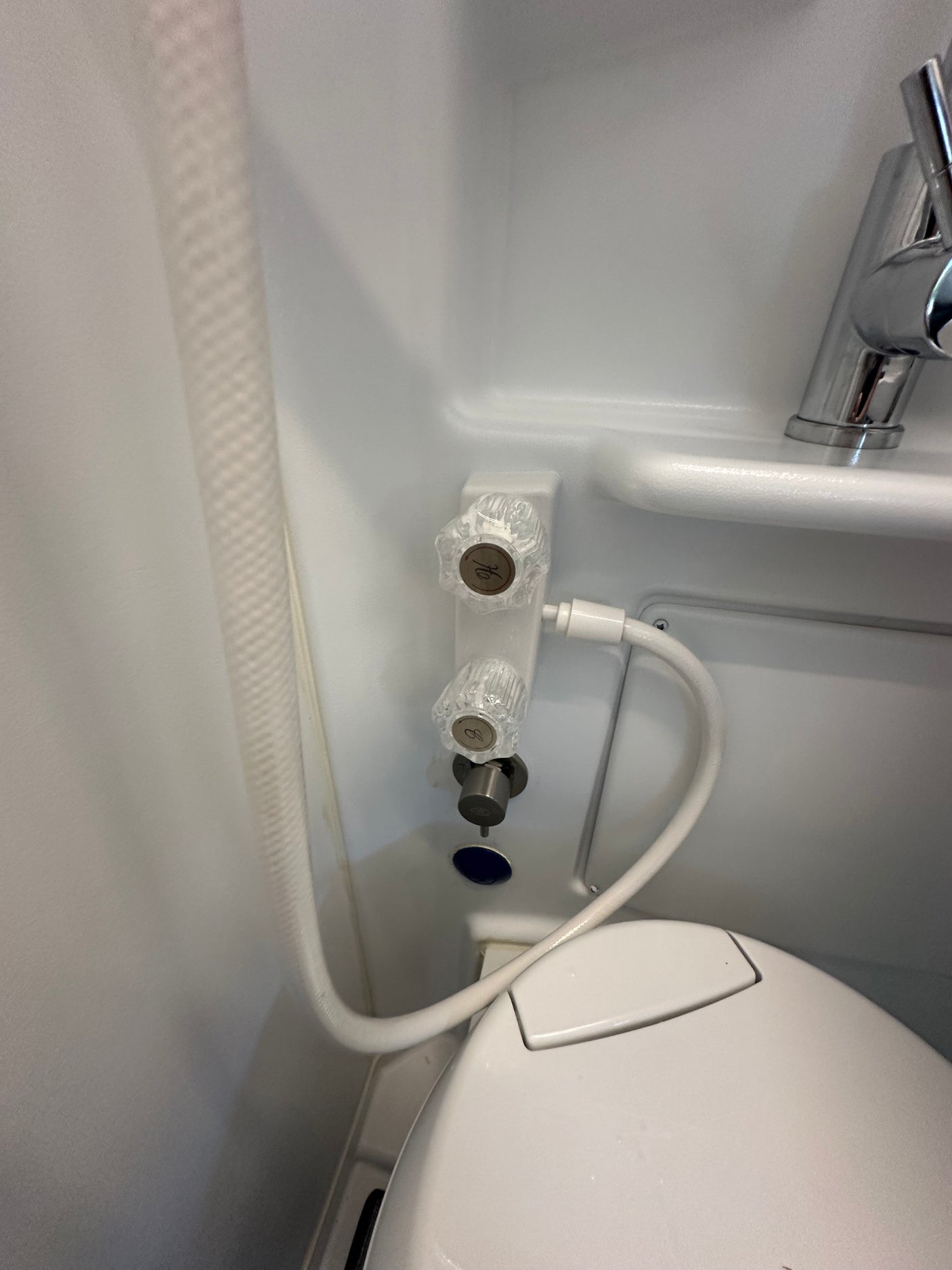 Compact RV rental wet bath with toilet, hot/cold shower controls, and flexible hose.