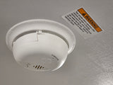Close-up of a white RV smoke alarm and a warning sticker, emphasizing testing for safety in an RV rental.