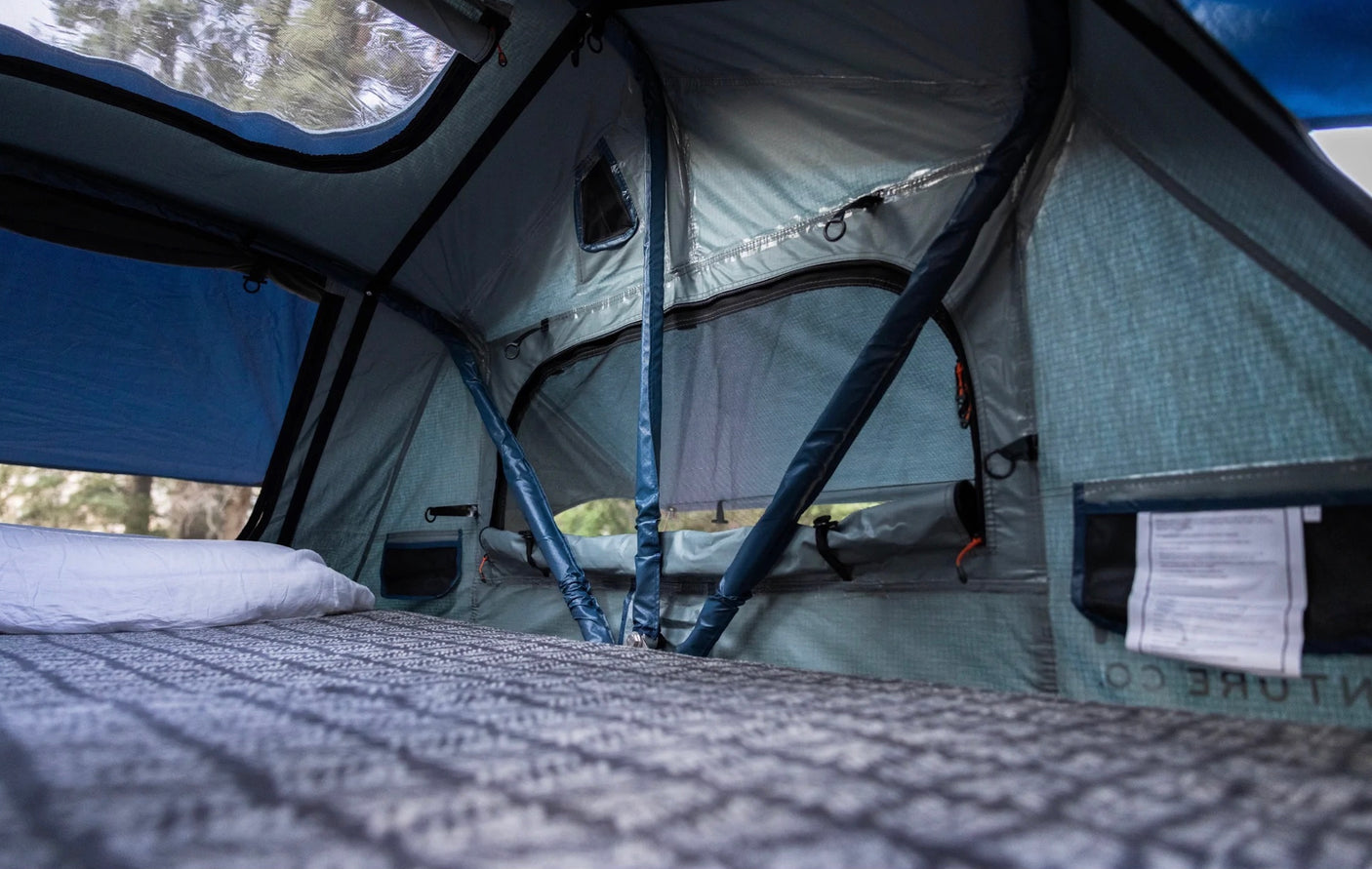RV rental sleeping area: a cozy tent interior with a bed, mesh windows & outdoor views.