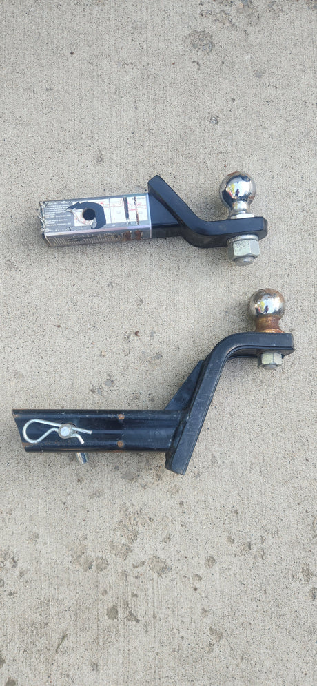 Trailer hitch ball mounts on concrete, essential for RV rental towing. Top has a label; bottom includes a pin.