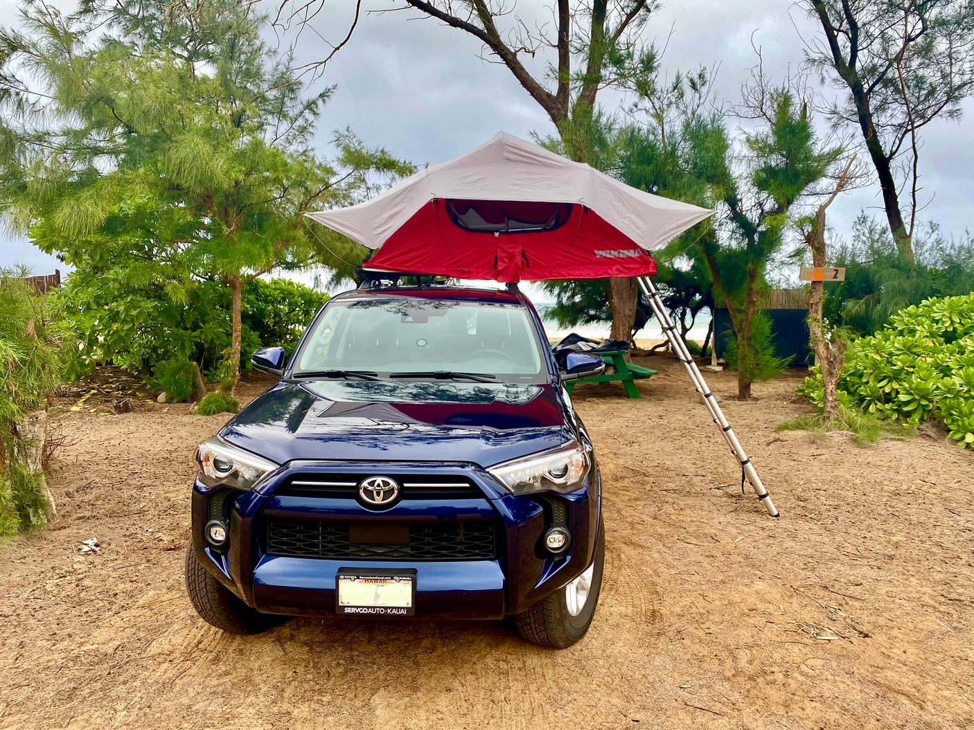 An RV rental alternative: a blue SUV with a rooftop tent set up for camping on a sandy beach. Site #2.
