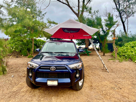 An RV rental alternative: a blue SUV with a rooftop tent set up for camping on a sandy beach. Site #2.