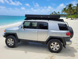 Silver FJ Cruiser with rooftop tent on a stunning beach, ideal for an RV rental adventure by the turquoise sea.