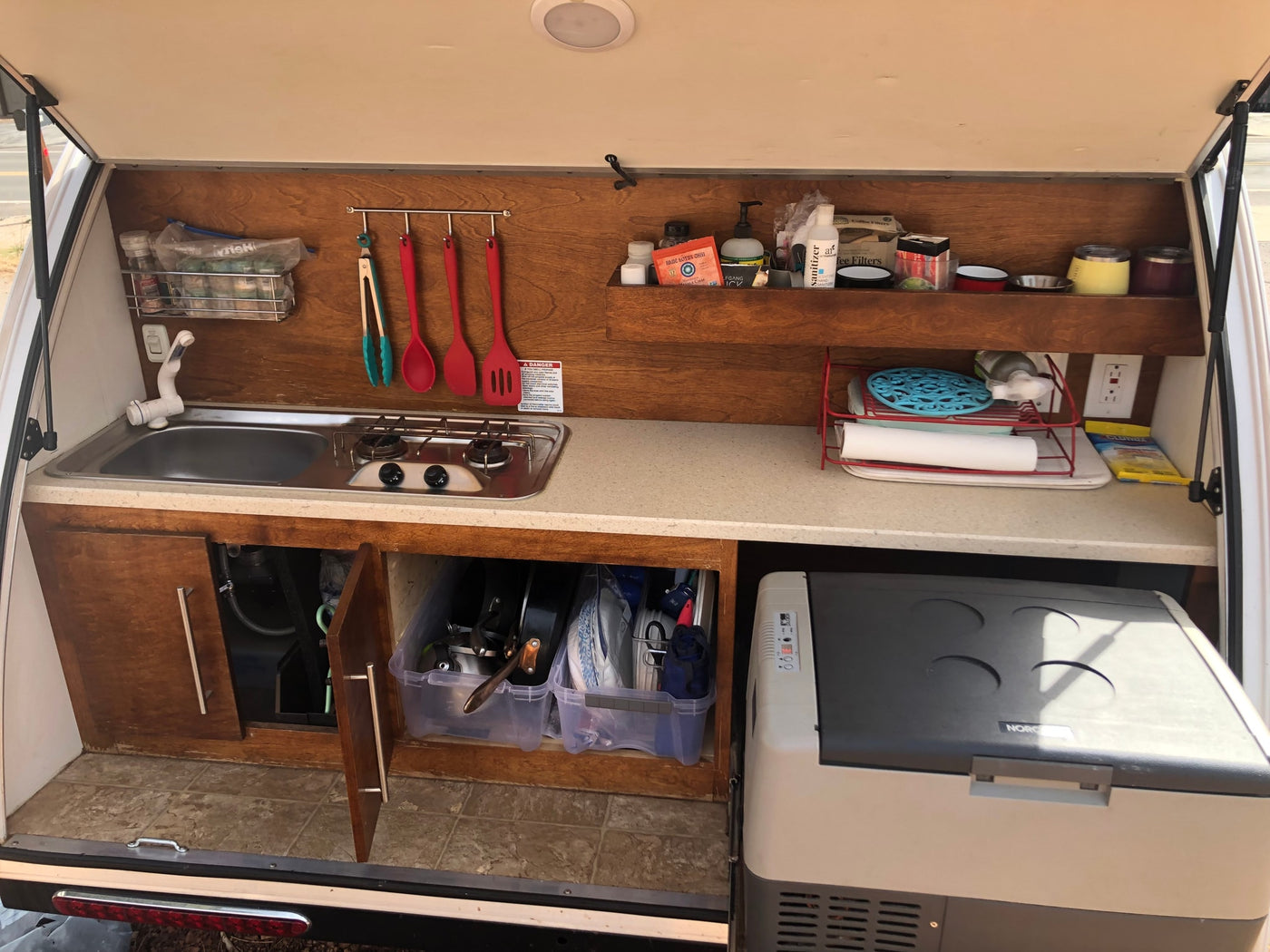 This organized RV rental kitchen features a sink, two-burner stove, portable fridge, and clever storage for cooking essentials. — photo 5