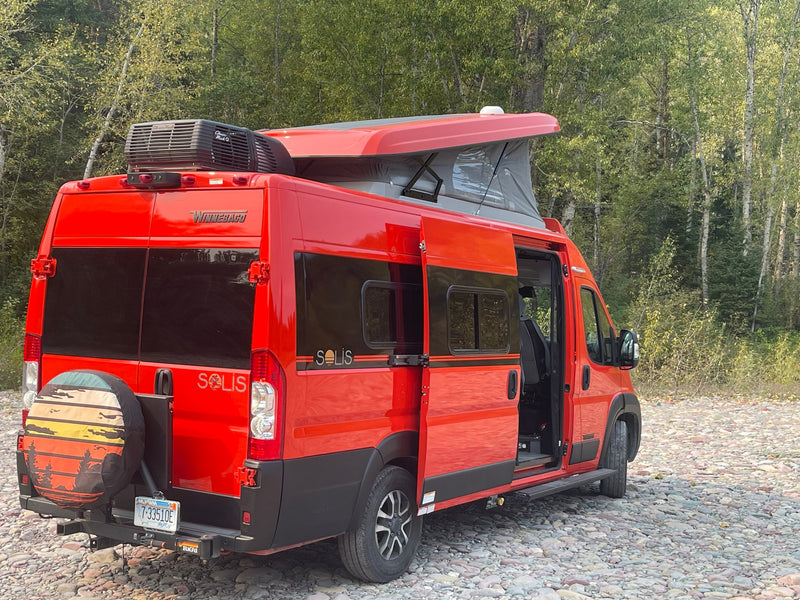  showcasing its versatile interior.|Bright orange Winnebago Solis pop-top camper van rv rental parked on a gravel riverbed near trees. Ready for adventure!|Red Winnebago Solis camper van for RV rental — photo 2