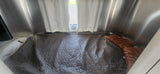 Inside a modern RV rental: a comfortable bed with a gray hexagonal quilt, orange pillows, and metallic walls for cozy travel.