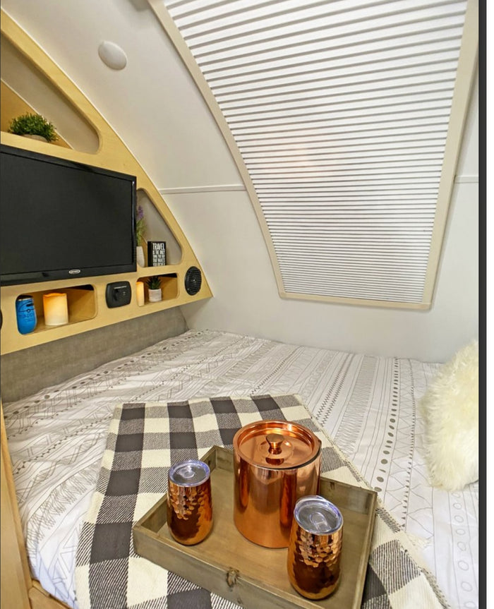 This cozy RV rental interior features a bed, entertainment setup, & copper amenities on a tray. Ready for your next travel adventure!