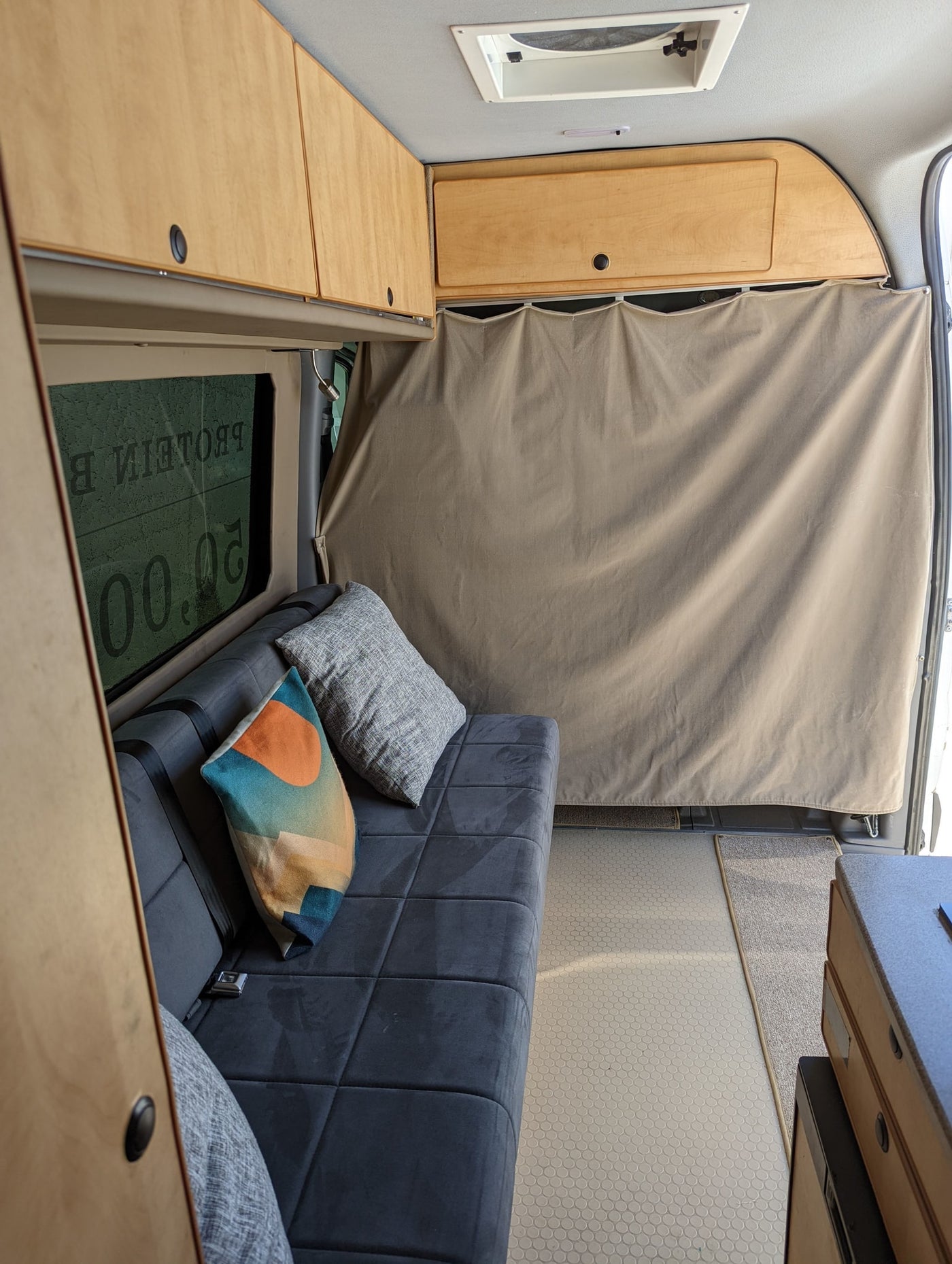 Spacious RV rental interior: overhead wooden cabinets, sofa with pillows, privacy curtain, and modern flooring for comfortable travel. — photo 9