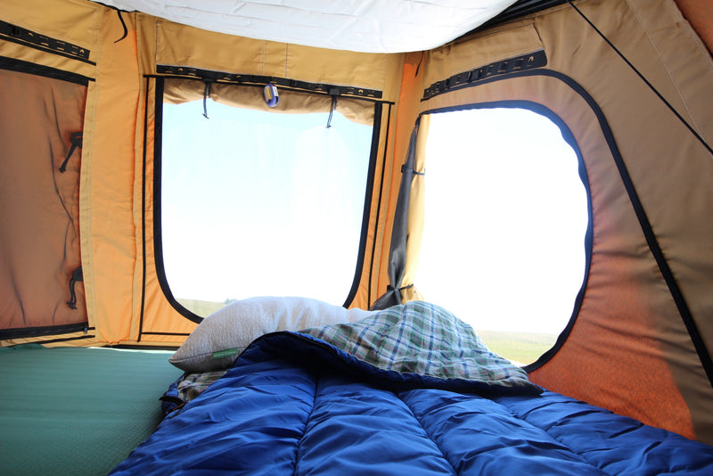 Cozy RV rental tent interior: green sleeping pad, blue sleeping bag, pillow, and a bright outdoor view through two windows. — photo 7