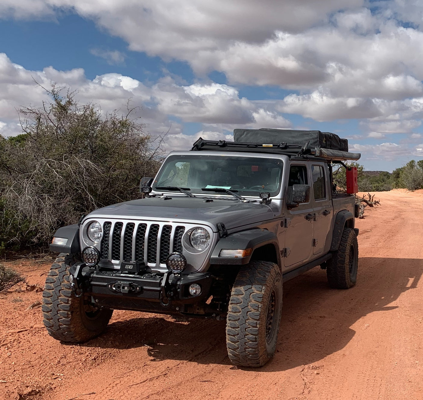 Off-road ready silver Jeep Gladiator with rooftop tent on a desert path. Perfect for an RV rental adventure.
