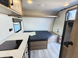 Compact RV rental interior featuring a kitchen with cooktop, sleeping area, and overhead storage, ideal for adventure.