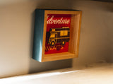 A decorative shadow box featuring an RV cutout and "Adventure AWAITS" message, perfect for inspiring your next RV rental trip.