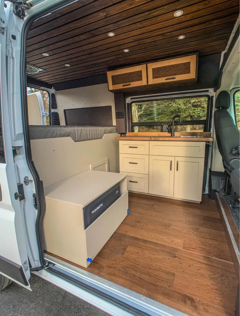Modern RV rental camper van interior. Features wood plank ceiling, full kitchen, bed area, and Dometic fridge on wood floors. — photo 7