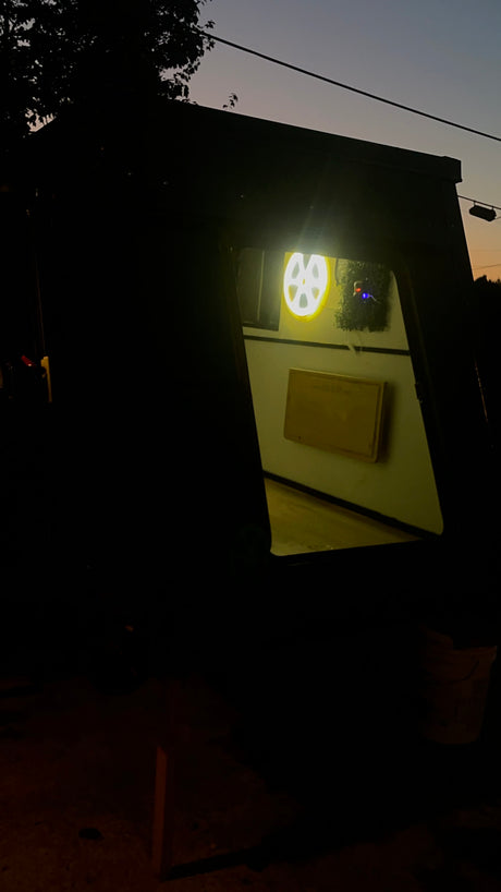 RV rental: Glowing gear light & wooden sign illuminate this cozy camper's interior, seen through its window at night.