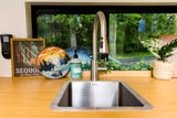 RV rental's inviting kitchen sink area, featuring a scenic window view, wooden counter, and nature-themed decor like an embroidered hoop.