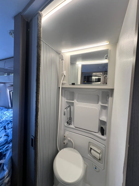 Compact RV rental wet bath features a toilet, shower, and lighted mirror. Maximizing space for travel.