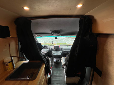 This cozy rv rental interior features a functional sink, front cockpit, and a stunning ocean view through the camper van windshield.