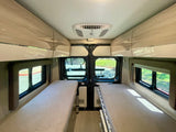 Interior view of an rv rental camper van, featuring two beds, overhead cabinets, and a ceiling AC unit for comfort.