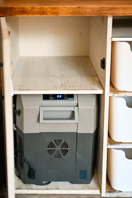 A portable fridge/freezer in a compact cabinet, shown with nearby storage bins, perfect for an rv rental.