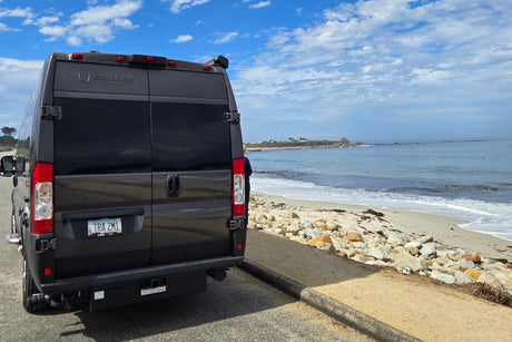 Gray Entegra Coach rv rental parked by a sunny beach and calm ocean. Perfect travel for beach trips under blue skies.