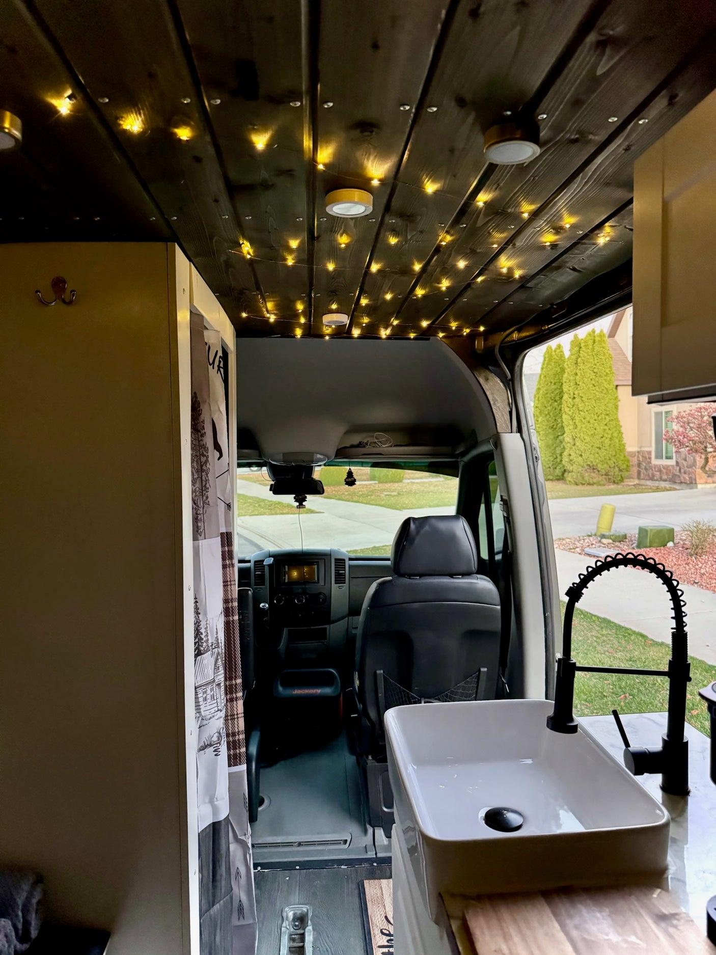 RV rental: Camper van interior. Custom wood ceiling with string lights, modern kitchen sink & dashboard view.