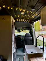RV rental: Camper van interior. Custom wood ceiling with string lights, modern kitchen sink & dashboard view.