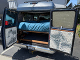 Step into this custom camper van conversion, an RV rental with a comfy bed, under-bed storage, and unique pebble-tiled doors.