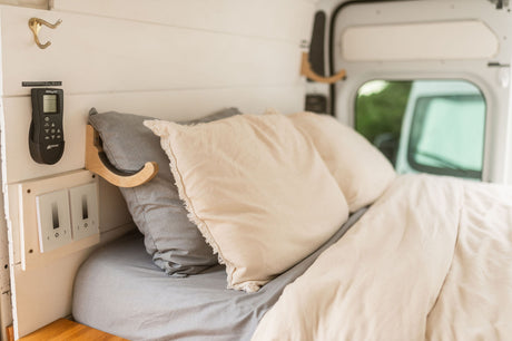 Cozy RV rental bedroom features a comfortable bed with pillows, a ventilation fan remote, and light controls on the wall.