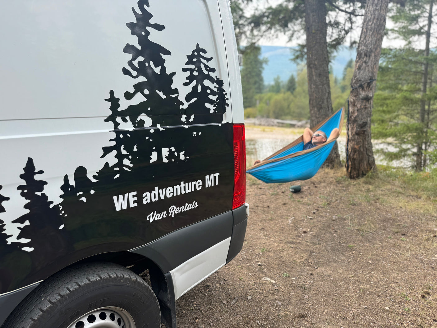 White RV rental van with tree graphics. A man enjoys a blue hammock by a scenic lake, showcasing adventure.