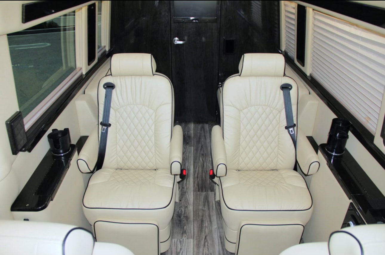 Premium rv rental interior: Two cream-colored, quilted leather captain seats with black piping, seatbelts, and side consoles. — photo 7