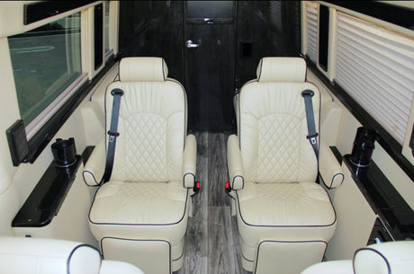 Premium rv rental interior: Two cream-colored, quilted leather captain seats with black piping, seatbelts, and side consoles.