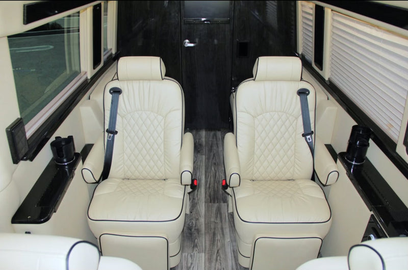 Premium rv rental interior: Two cream-colored, quilted leather captain seats with black piping, seatbelts, and side consoles. — photo 7