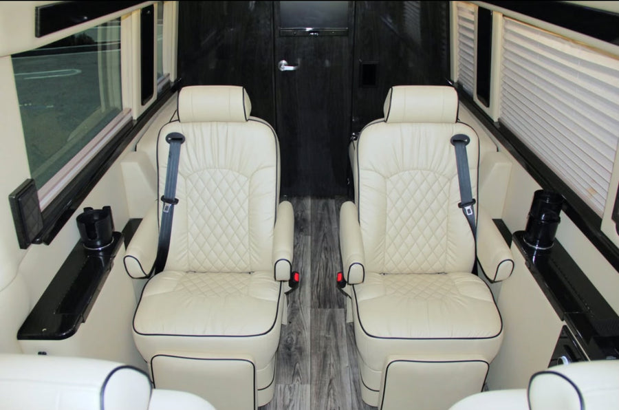 Premium rv rental interior: Two cream-colored, quilted leather captain seats with black piping, seatbelts, and side consoles.
