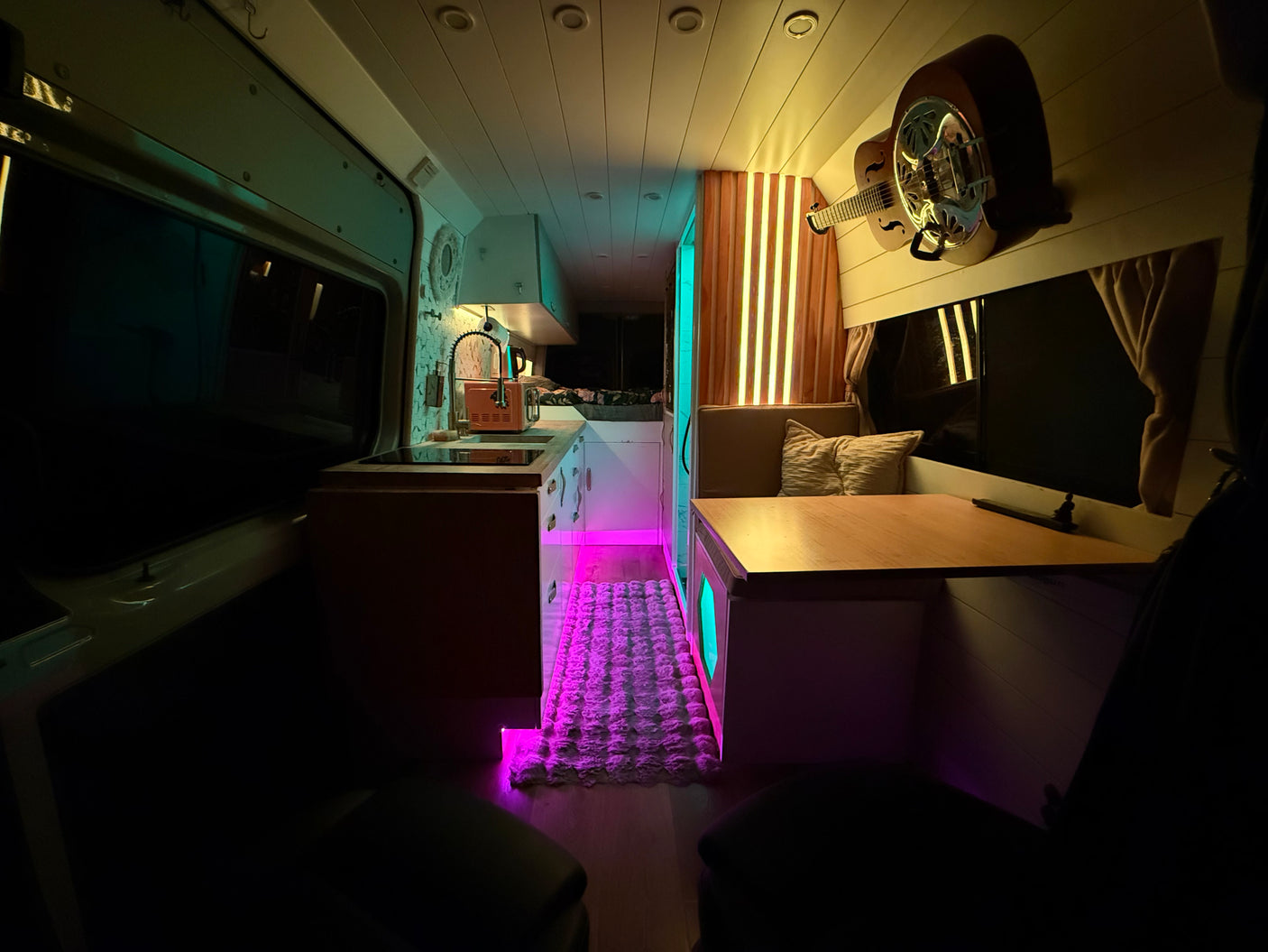 Cozy rv rental interior featuring a kitchen area, dining nook, wall-mounted guitar, and vibrant custom LED lighting.