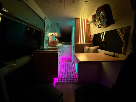 Cozy rv rental interior featuring a kitchen area, dining nook, wall-mounted guitar, and vibrant custom LED lighting.