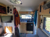 This RV rental interior showcases a compact kitchenette, TV, and cozy living space, ideal for travel adventures.