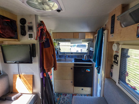 This RV rental interior showcases a compact kitchenette, TV, and cozy living space, ideal for travel adventures.