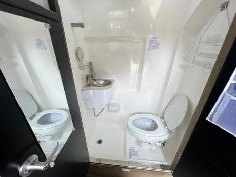 Compact RV rental bathroom featuring an integrated toilet, sink, and shower in a single unit.