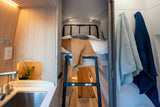 Modern rv rental camper van interior. Features a compact kitchen, comfortable bunk bed with ladder, and bathroom towels.
