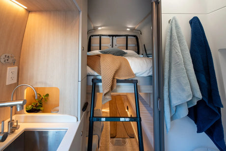 Modern rv rental camper van interior. Features a compact kitchen, comfortable bunk bed with ladder, and bathroom towels.